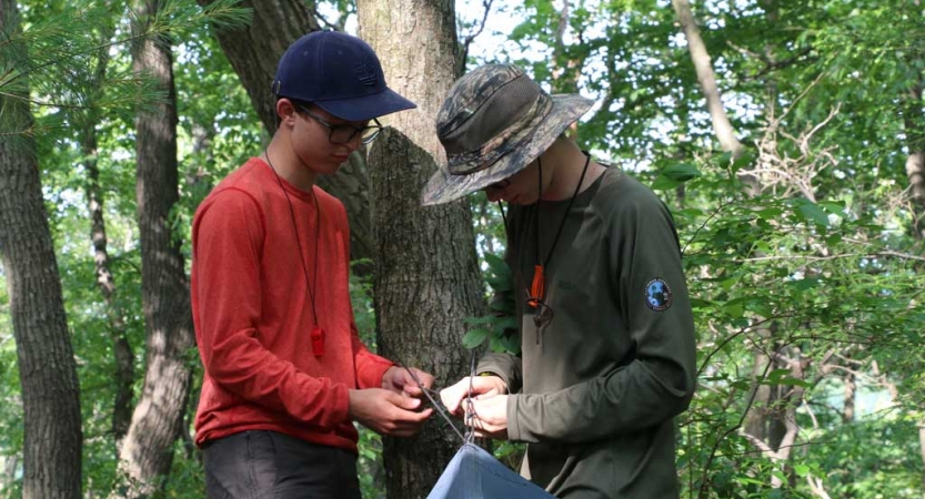 Two people work to secure a tarp shelter to a tree